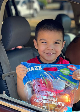 A boy looking out a car window holding a bag of apples