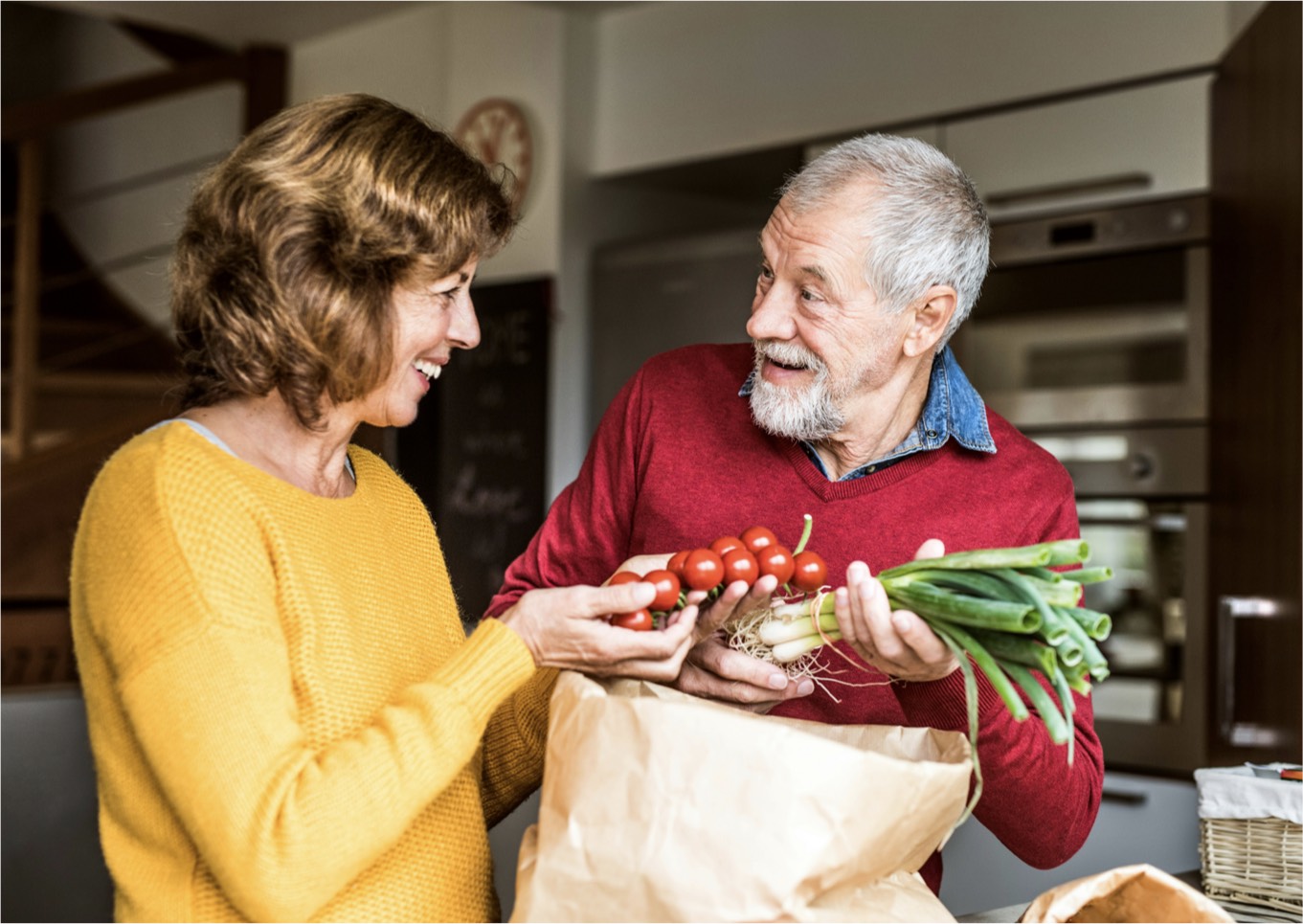 A couple pulling produce out of a bag in the kitchen
